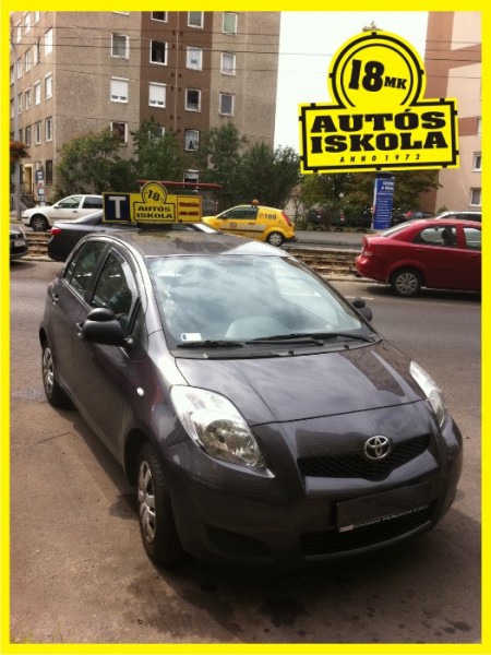 Toyota Yaris oktatóautó tanuló-tetőtáblával az autósiskola irodája előtt